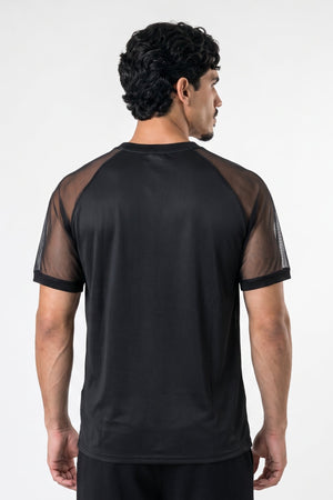 A man viewed from the back wearing a black athletic t-shirt with sheer mesh raglan sleeves, set against a plain light gray studio background.