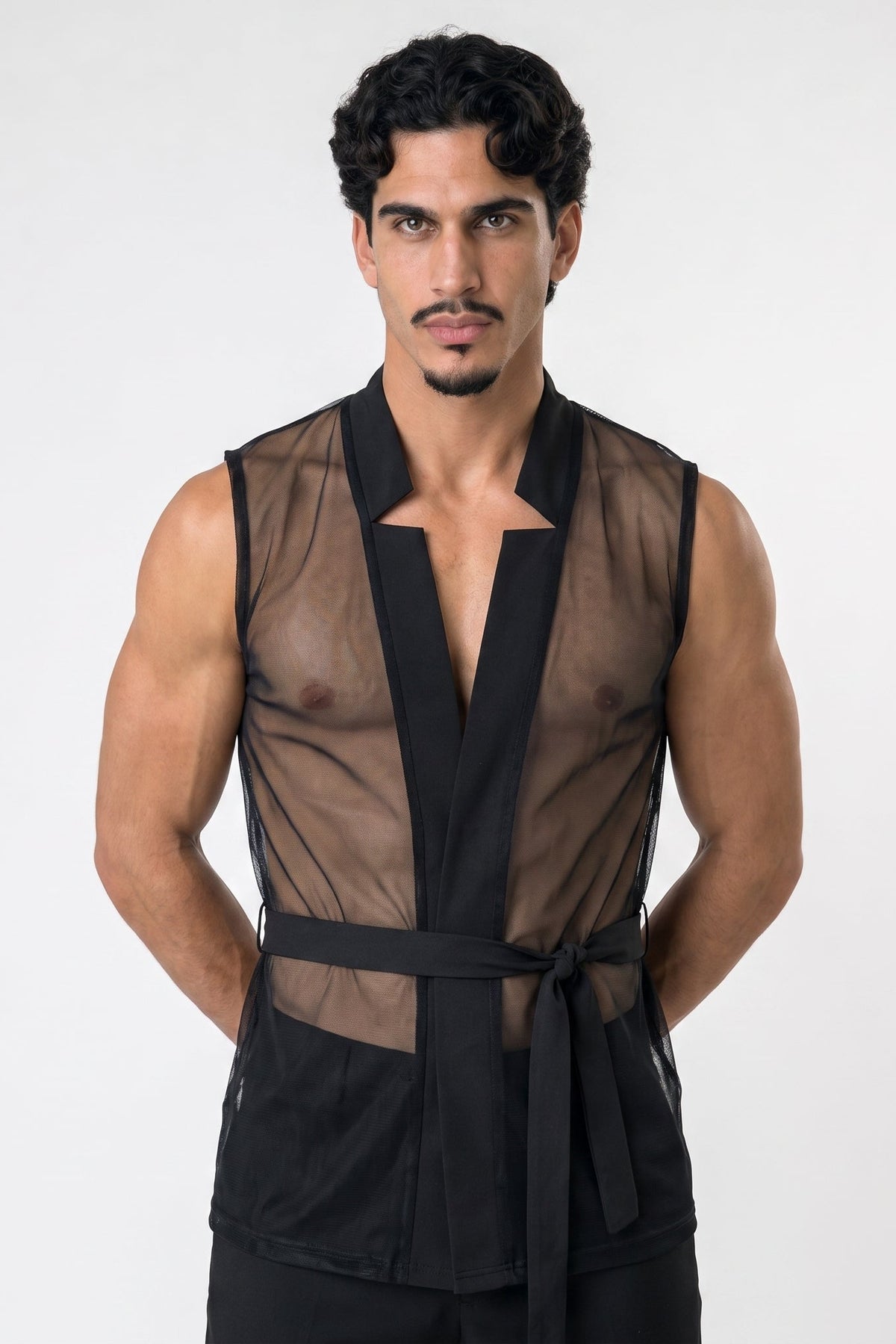 A man modeling a black sheer mesh wrap-style vest with a tie belt, photographed against a plain light gray studio background.