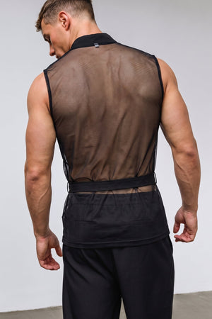 A man shown from the back wearing a black sleeveless mesh vest over black athletic shorts, photographed in a studio setting against a light gray wall.