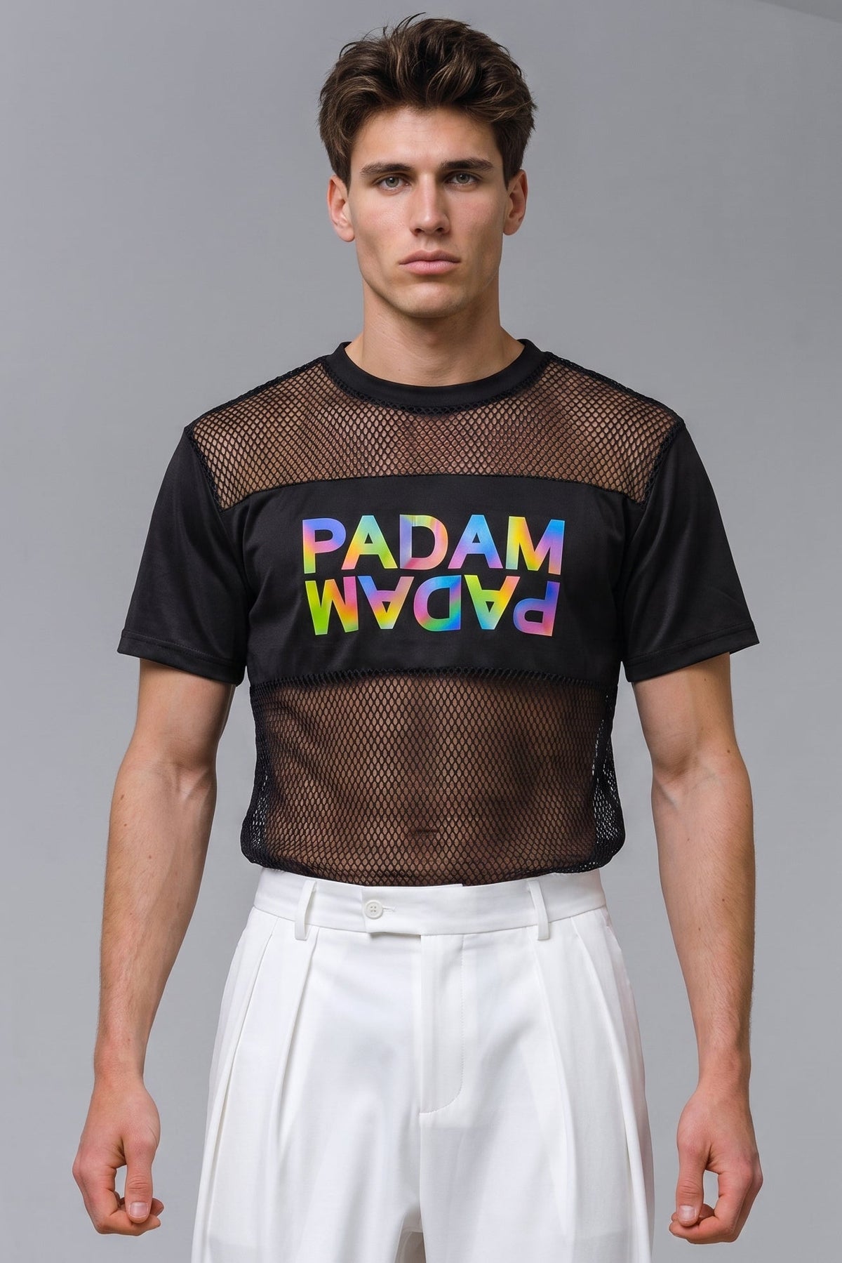 A male model wearing a black short-sleeve mesh crop top with a colorful 'PADAM' graphic on the chest, paired with white trousers, against a plain gray studio background.