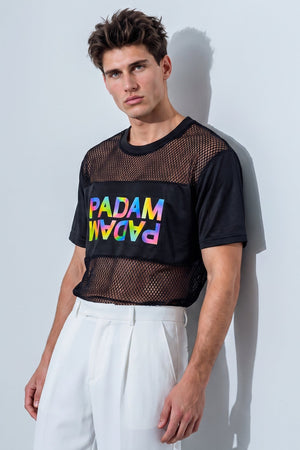 A male model wearing a black short-sleeve mesh crop top with a colorful 'PADAM' graphic on the chest, paired with white trousers, standing against a light gray wall.