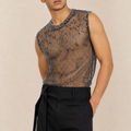 A man wearing a sleeveless black mesh top with a snakeskin pattern and black trousers, standing against a plain beige background.